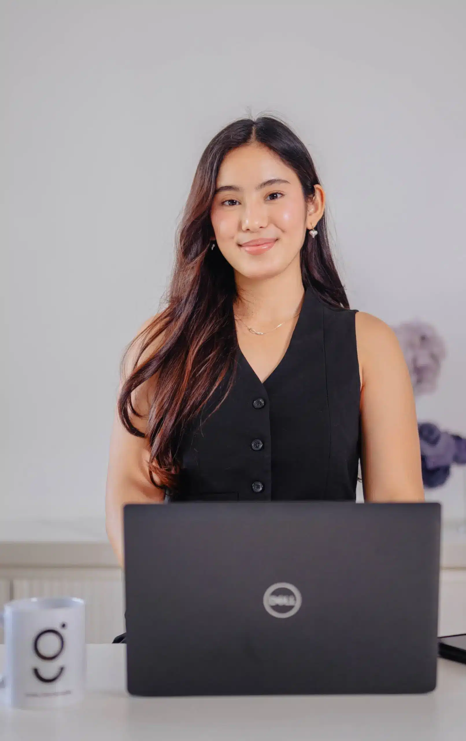 Smiling woman in business attire sitting at a desk working on a laptop, representing remote staffing services